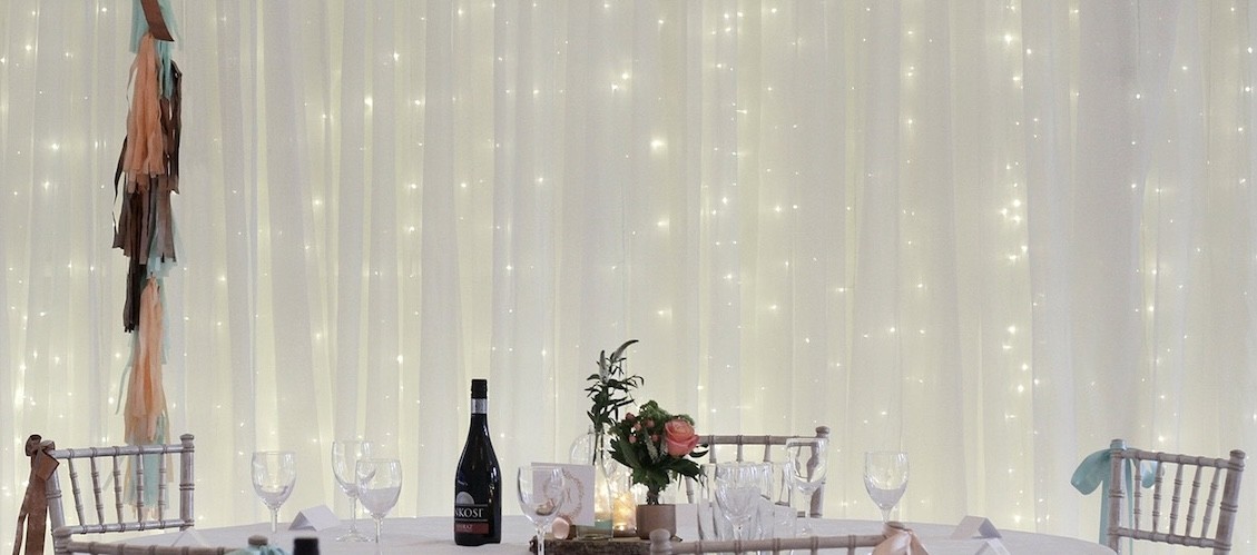 Fairy-light curtain backdrop and candlelit tables dressed for a wedding reception